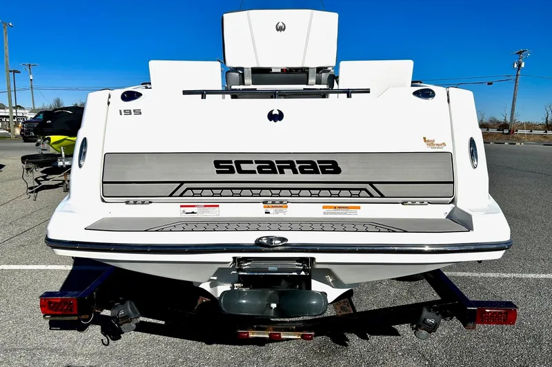 Slide: The Image of 2021 Scarab 195 ID boat rear view, parked on a trailer in a sunny outdoor setting. - 10