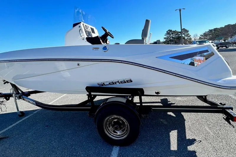 Slide: The Image of 2021 Scarab 195 ID boat on trailer, side view, in a parking lot under clear blue sky. - 8