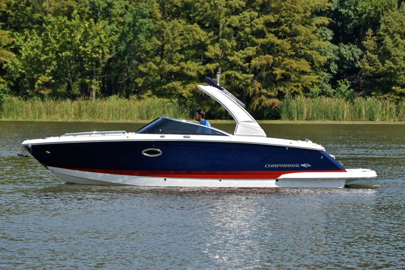 Slide: The Image of 2019 Chaparral 277 SSX boat cruising on a calm lake with lush green trees. - 11