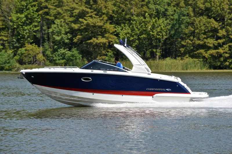 Slide: The Image of 2019 Chaparral 277 SSX boat cruising on a lake with lush green trees. - 2