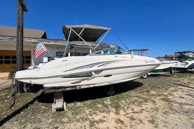 The Image of 2004 Sea Ray 220 Sundeck boat on dry land with American flag, clear blue sky. - 0