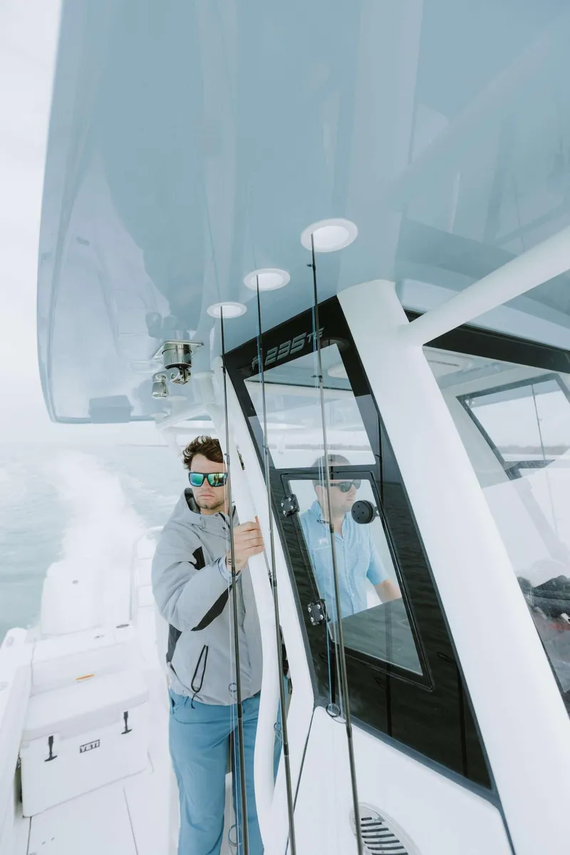 Slide: The Image of Man on 2026 World Cat 235TE boat, wearing sunglasses, navigating on open water. - 15