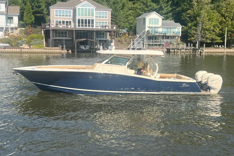 The Image of 2020 Scout 380 LXF boat cruising on a lake near waterfront homes. - 0