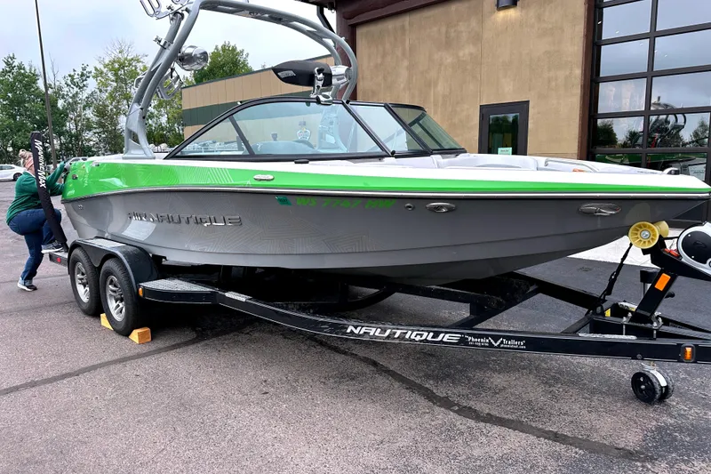 Slide: The Image of 2012 Nautique Sport Nautique 200 boat on trailer, green and gray design, parked outdoors. - 1