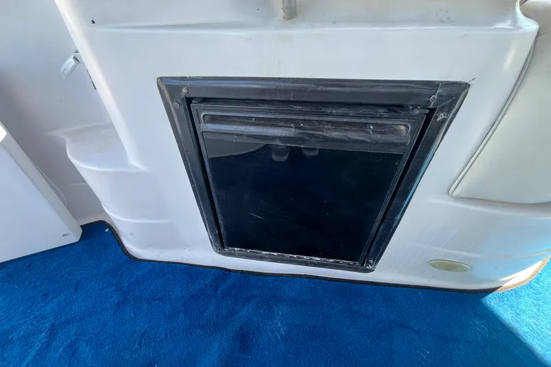 Slide: The Image of 2005 Larson-Cabrio 370 boat interior with built-in black refrigerator on blue carpet. - 15
