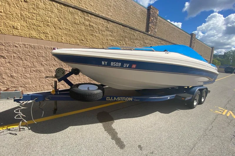 Slide: The Image of 1998 Glastron/Carlson GS225 boat on trailer, blue cover, parked by brick wall. - 2