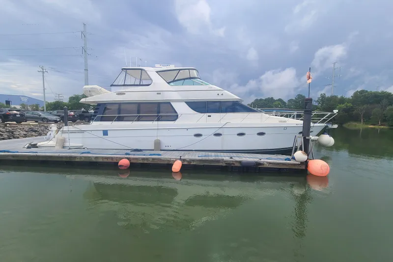 Slide: The Image of 2004 Carver 570 Voyager Pilothouse yacht docked on a calm lake under cloudy skies. - 86