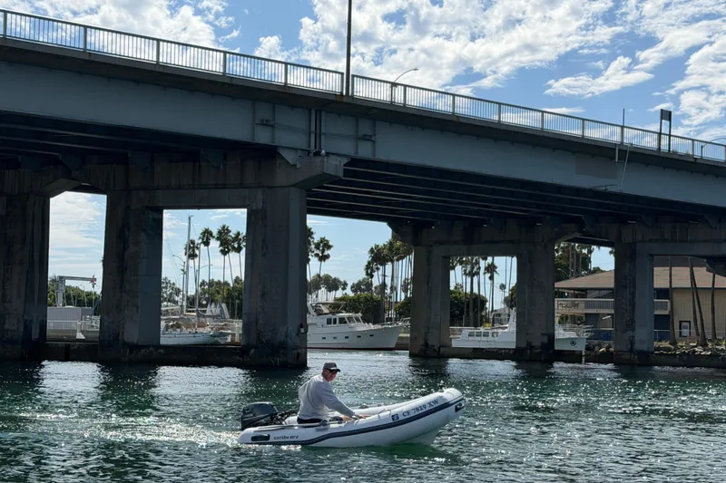 Slide: The Image of Man in a small boat under a bridge, sunny day, palm trees in background. - 42