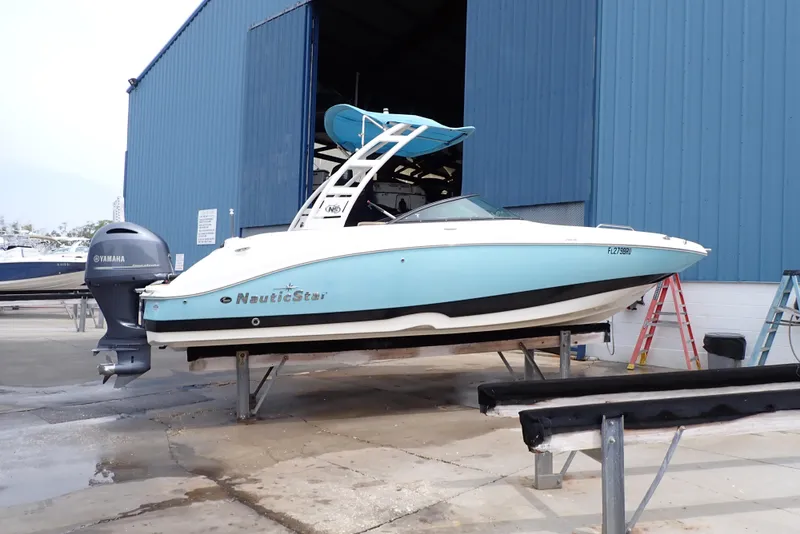 Slide: The Image of 2019 NauticStar 243DC Sport Deck boat on dry dock near blue warehouse. - 0
