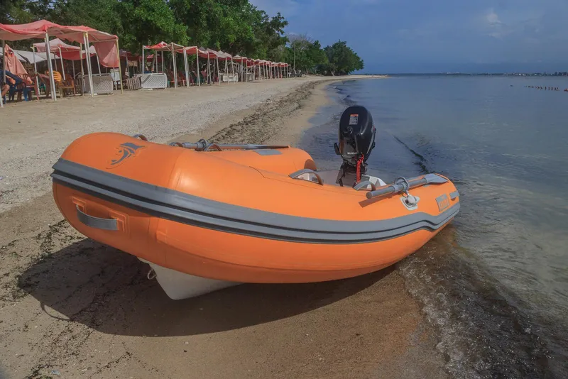 Slide: The Image of Orange inflatable boat on sandy beach with calm sea and distant trees. - 7