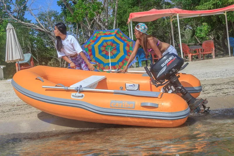 Slide: The Image of Two people with an orange Caribe L9 inflatable boat on a sunny beach. - 8