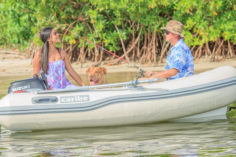 Slide: The Image of People and dog fishing on a Caribe C9X boat, 2025 model, near lush greenery. - 6