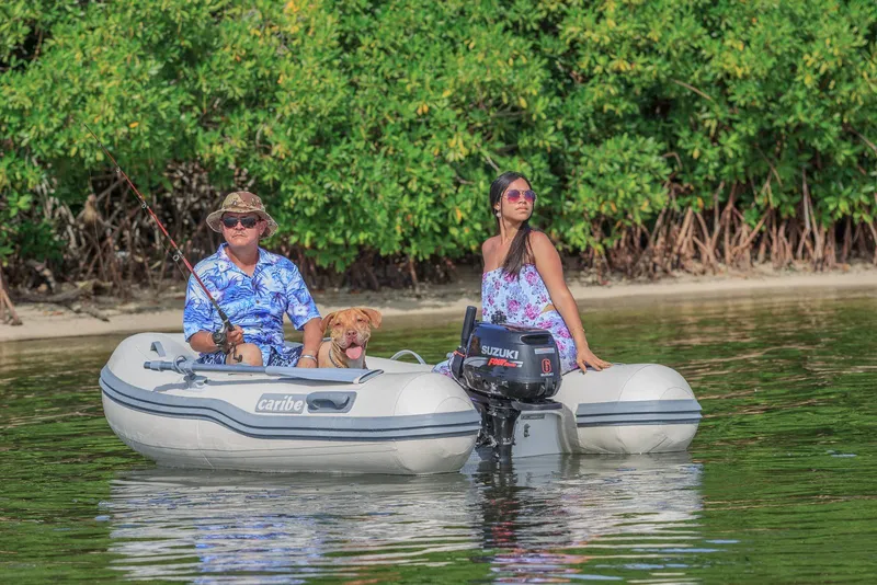 Slide: The Image of Man, woman, and dog on a Caribe C9X inflatable boat, 2025 model, fishing near lush greenery. - 7