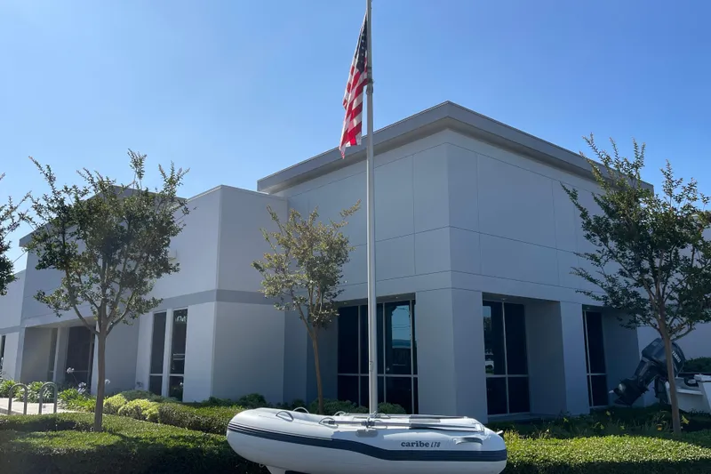 Slide: The Image of Modern building with flagpole, trees, and a 2025 Caribe L8 inflatable boat displayed in front. - 30
