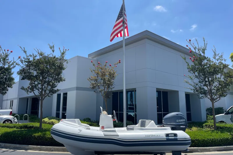 Slide: The Image of Inflatable Caribe DL11 boat parked outside modern building with American flag, 2025 model. - 2