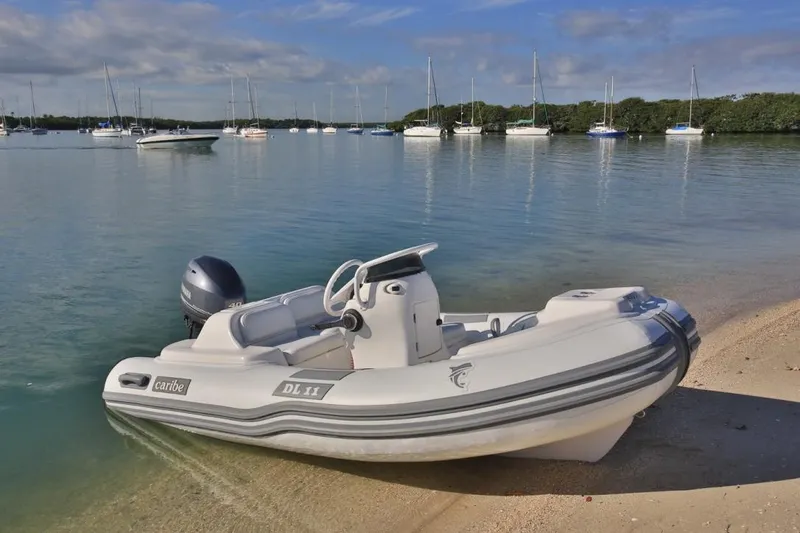 Slide: The Image of 2025 Caribe DL11 inflatable boat on sandy beach with sailboats in background. - 41