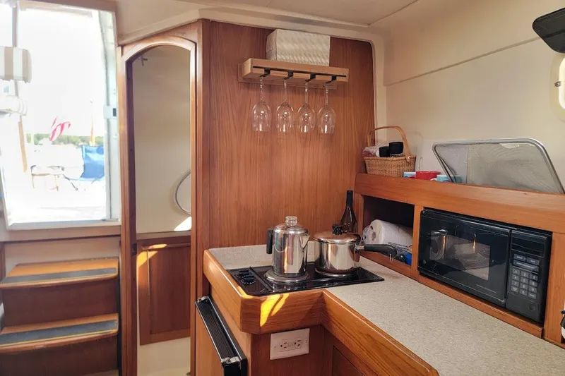Slide: The Image of Mainship 34 PILOT 2000 boat interior kitchen with stove, microwave, and wooden cabinetry. - 11