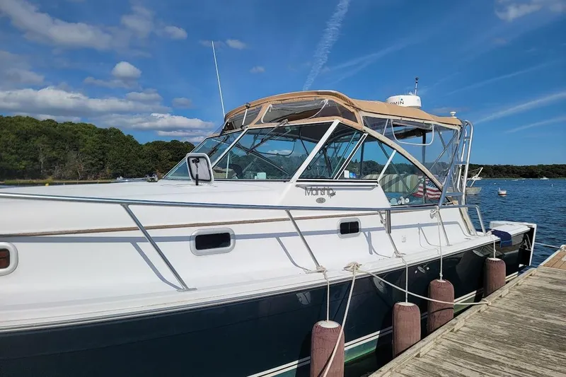 Slide: The Image of 2000 Mainship 34 PILOT yacht docked by a scenic shoreline under a clear blue sky. - 32