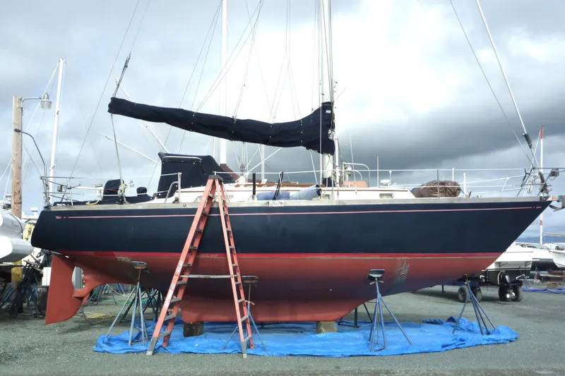 Slide: The Image of 1987 Bristol 35.5 sailboat on land with ladder and tarp, cloudy sky background. - 3