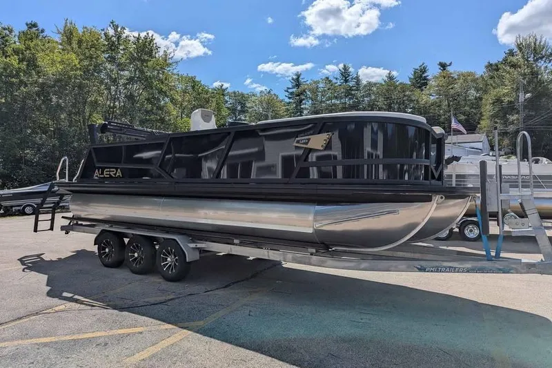 Slide: The Image of 2026 Alera M23L pontoon boat on trailer, parked outdoors under a clear sky. - 0
