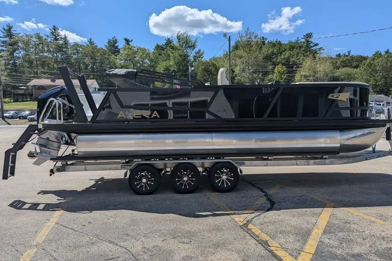 Slide: The Image of 2026 Alera M23L pontoon boat on a trailer, parked outdoors under a clear sky. - 1