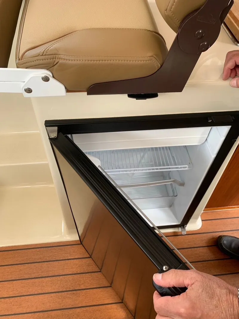 Slide: The Image of 2020 Ranger Tugs R-25 interior with open mini fridge and tan seating. - 32