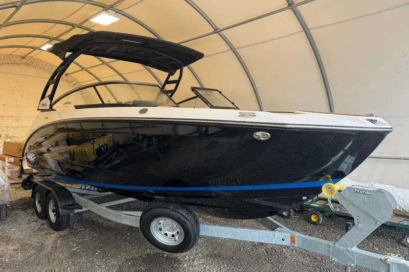 The Image of 2026 Yamaha Boats 252SD in storage, sleek black design on trailer. - 0