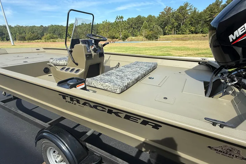 Slide: The Image of 2026 Tracker Grizzly 2072 CC boat with camouflage seating and Mercury engine, parked outdoors. - 2