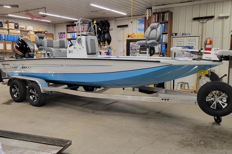 The Image of 2026 Xpress H22B Bay boat in a garage, featuring a sleek design and dual-axle trailer. - 1