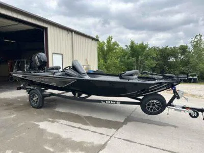 Slide: The Image of 2025 Lowe Stinger 175 Crappie boat on trailer, parked outside a garage. - 2