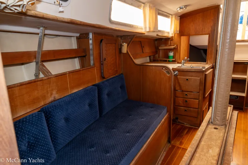 Slide: The Image of 1984 Sabre 32 Aft-Cabin interior with blue sofa, wooden cabinetry, and compact kitchen area. - 53