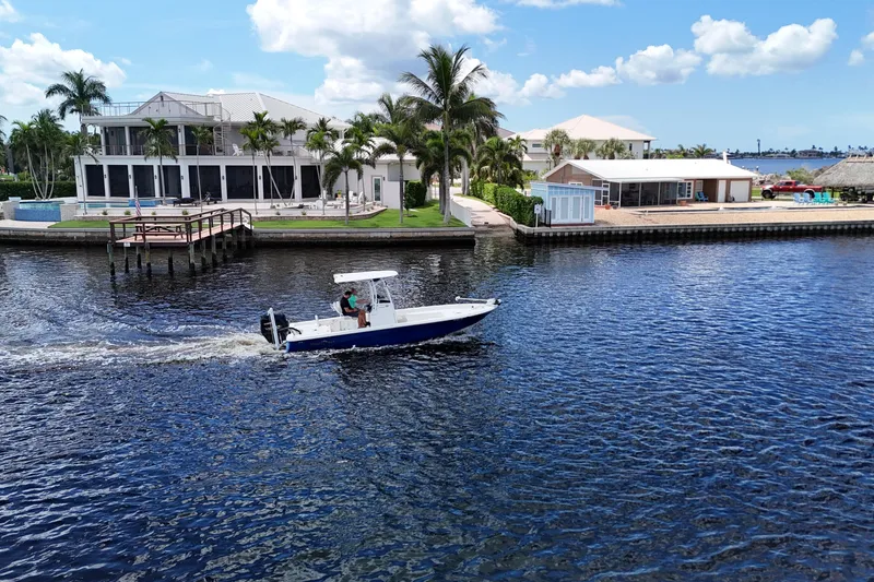 Slide: The Image of 2017 NauticStar 244 XTS boat cruising on a scenic waterfront with palm trees and luxury homes. - 21