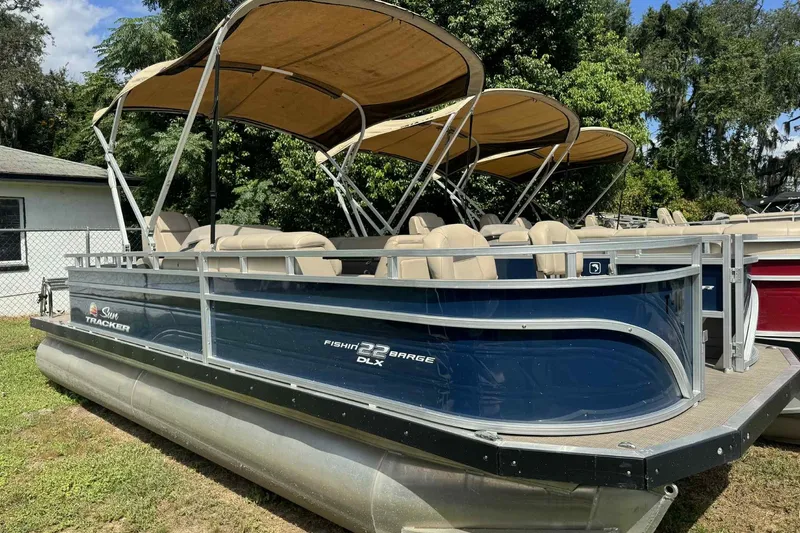 The Image of 2024 Sun Tracker Fishin' Barge 22 DLX pontoon boat with canopy, parked outdoors. - 0