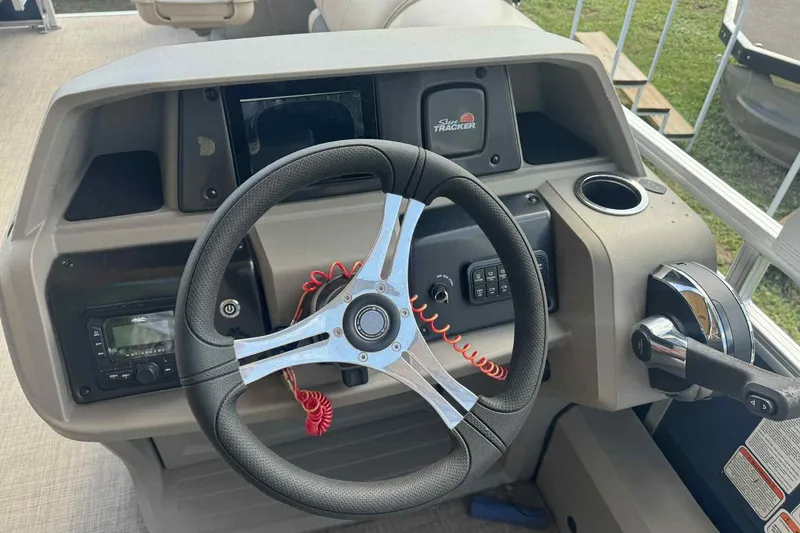 Slide: The Image of 2024 Sun Tracker Fishin' Barge 22 DLX steering console with modern controls and cup holder. - 2