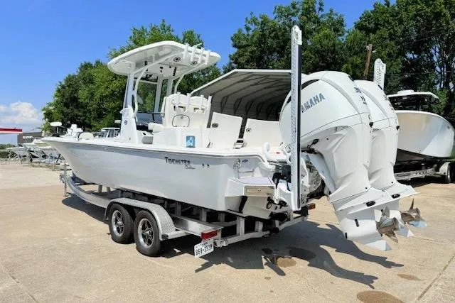 Slide: The Image of 2024 Tidewater 2700 Carolina Bay boat on trailer, featuring dual engines, parked outdoors. - 2