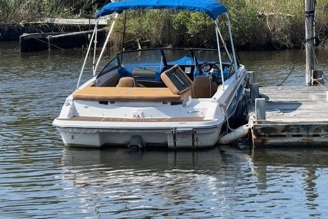 Slide: The Image of 2019 Glastron GT 205 boat docked on calm water with blue canopy. - 2