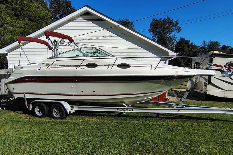 Slide: The Image of 1995 Sea Ray 250 Sundancer boat on trailer, parked beside a white house. - 8