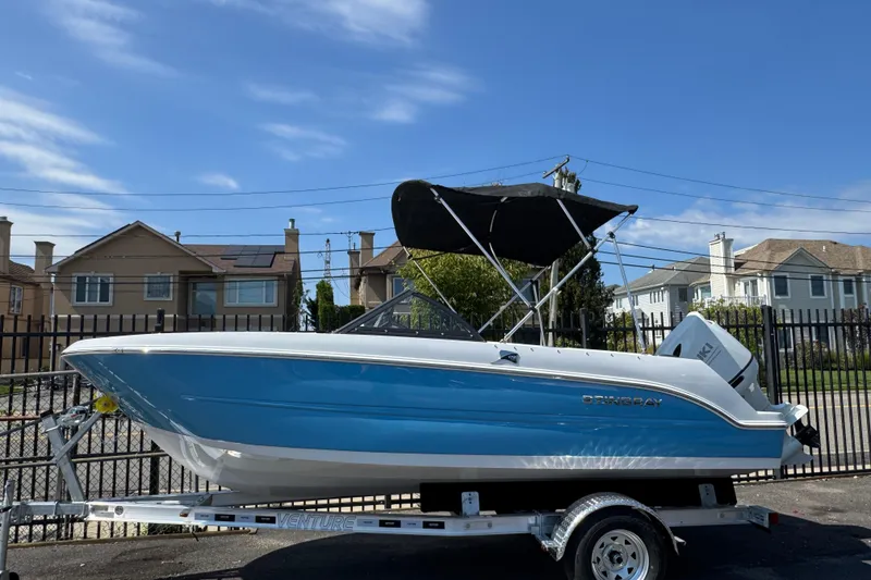 The Image of 2026 Stingray 172 SC boat on trailer, blue hull, black canopy, residential background. - 0
