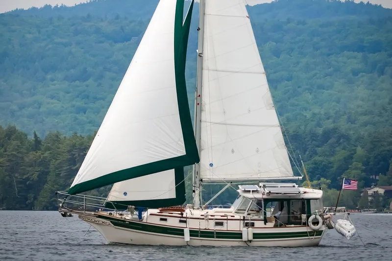 The Image of Sailboat Gozzard 31, 1991 model, cruising on a scenic lake with forested hills. - 1