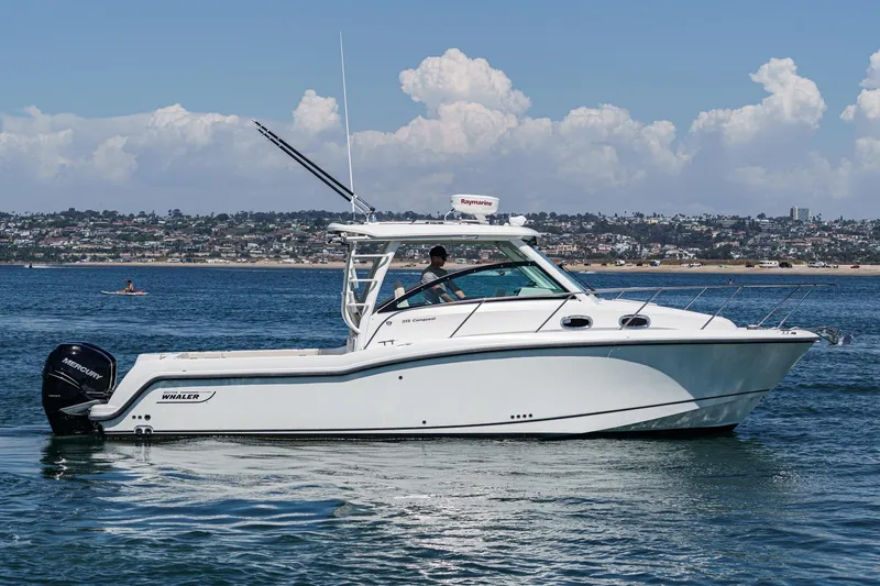 Slide: The Image of 2018 Boston Whaler 315 Conquest boat cruising on calm waters with cityscape background. - 0