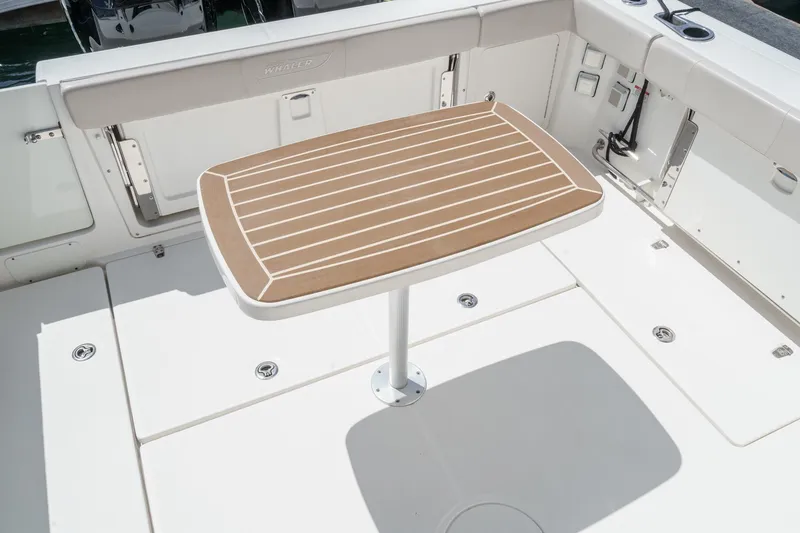 Slide: The Image of 2018 Boston Whaler 315 Conquest deck with wooden table, white seating, and storage compartments. - 12