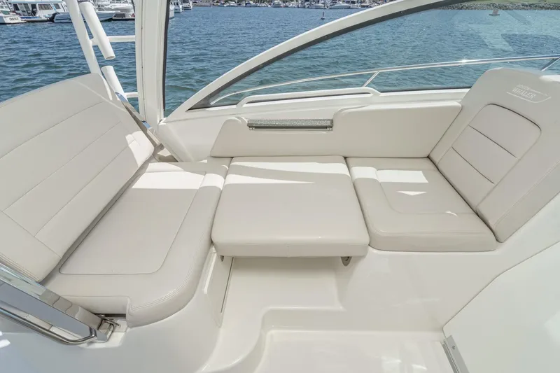 Slide: The Image of 2018 Boston Whaler 315 Conquest interior seating with white cushions, docked by the water. - 26