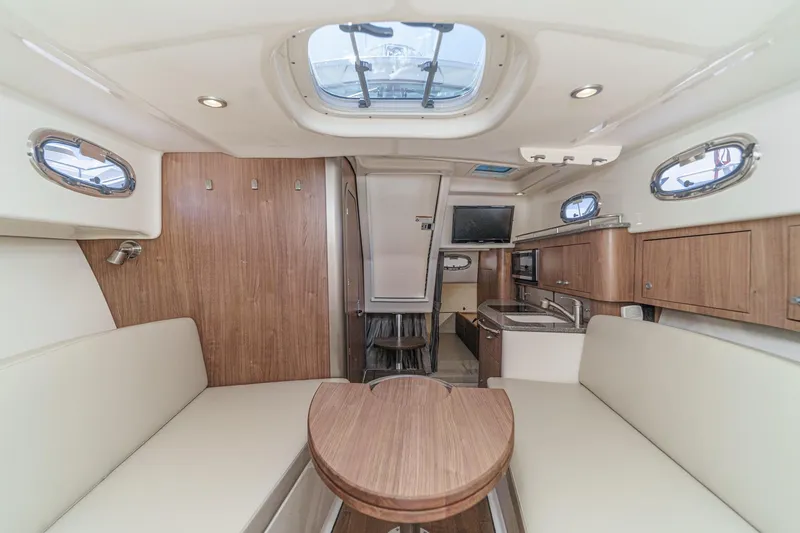 Slide: The Image of Interior of 2018 Boston Whaler 315 Conquest, featuring seating, kitchenette, and portholes. - 34