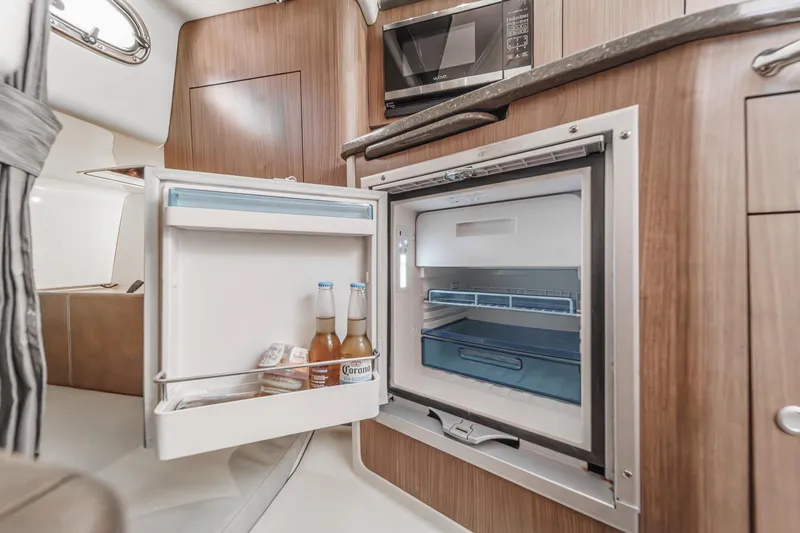 Slide: The Image of 2018 Boston Whaler 315 Conquest cabin with open fridge, wooden cabinetry, and microwave. - 36