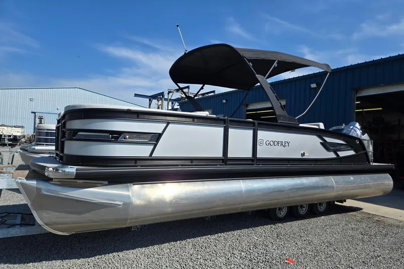The Image of 2026 Godfrey AquaPatio 255 SFL pontoon boat with sleek design and canopy, parked outdoors. - 0