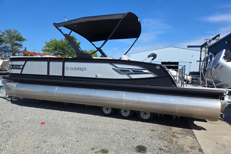 Slide: The Image of 2026 Godfrey AquaPatio 255 SFL pontoon boat with black canopy on display outdoors. - 2