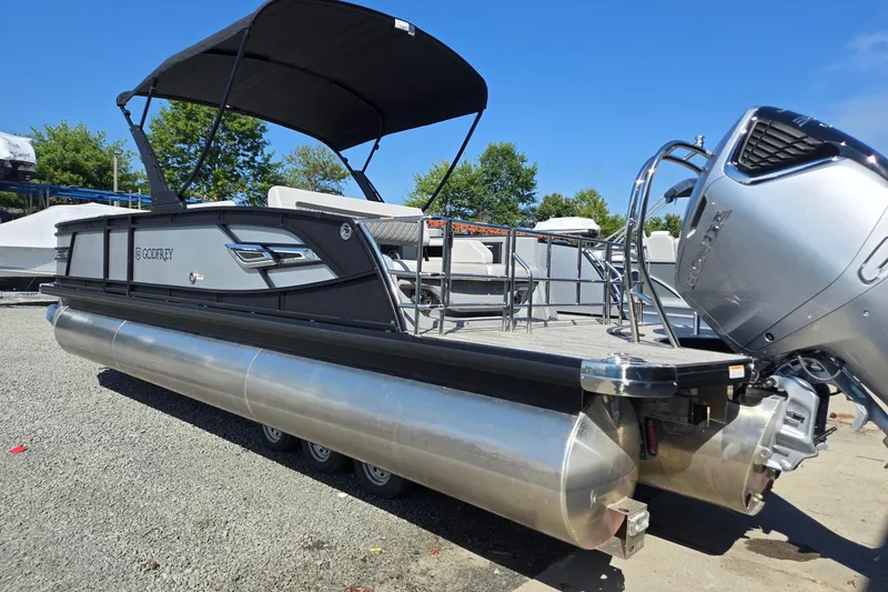Slide: The Image of 2026 Godfrey AquaPatio 255 SFL pontoon boat with canopy and outboard motor, parked on gravel. - 3