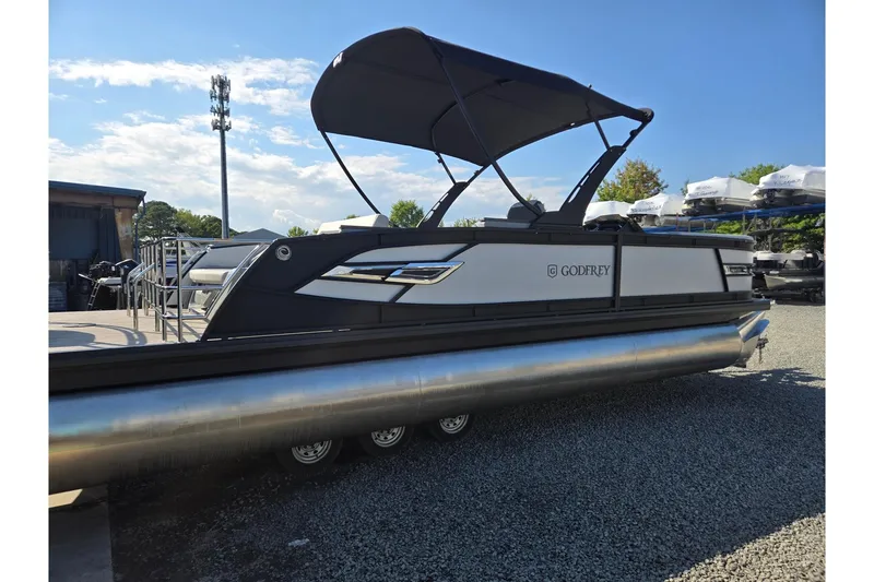 Slide: The Image of 2026 Godfrey AquaPatio 255 SFL pontoon boat with canopy, parked on gravel. - 6