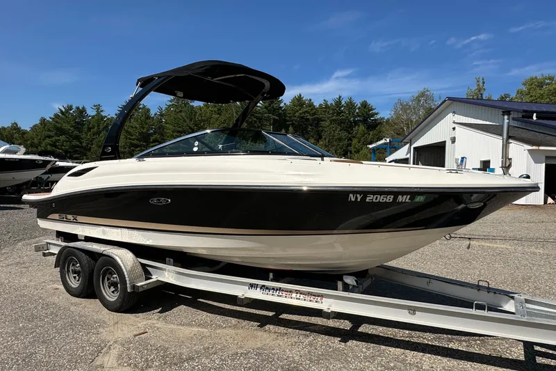 Slide: The Image of 2015 Sea Ray 230 SLX boat on trailer, parked outdoors near trees and buildings. - 7