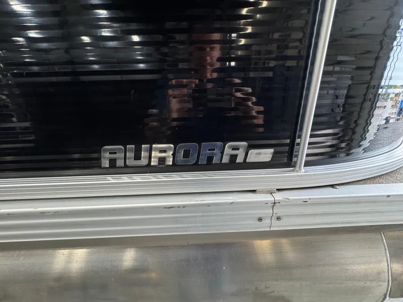 Slide: The Image of 2018 Manitou 21 Aurora LE Standard boat logo on dark metallic surface. - 24